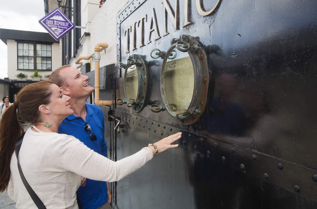 Des visiteurs souriants touchent l'extérieur en acier noir et les hublots de l'exposition Titanic Experience au centre du patrimoine à Cobh.
