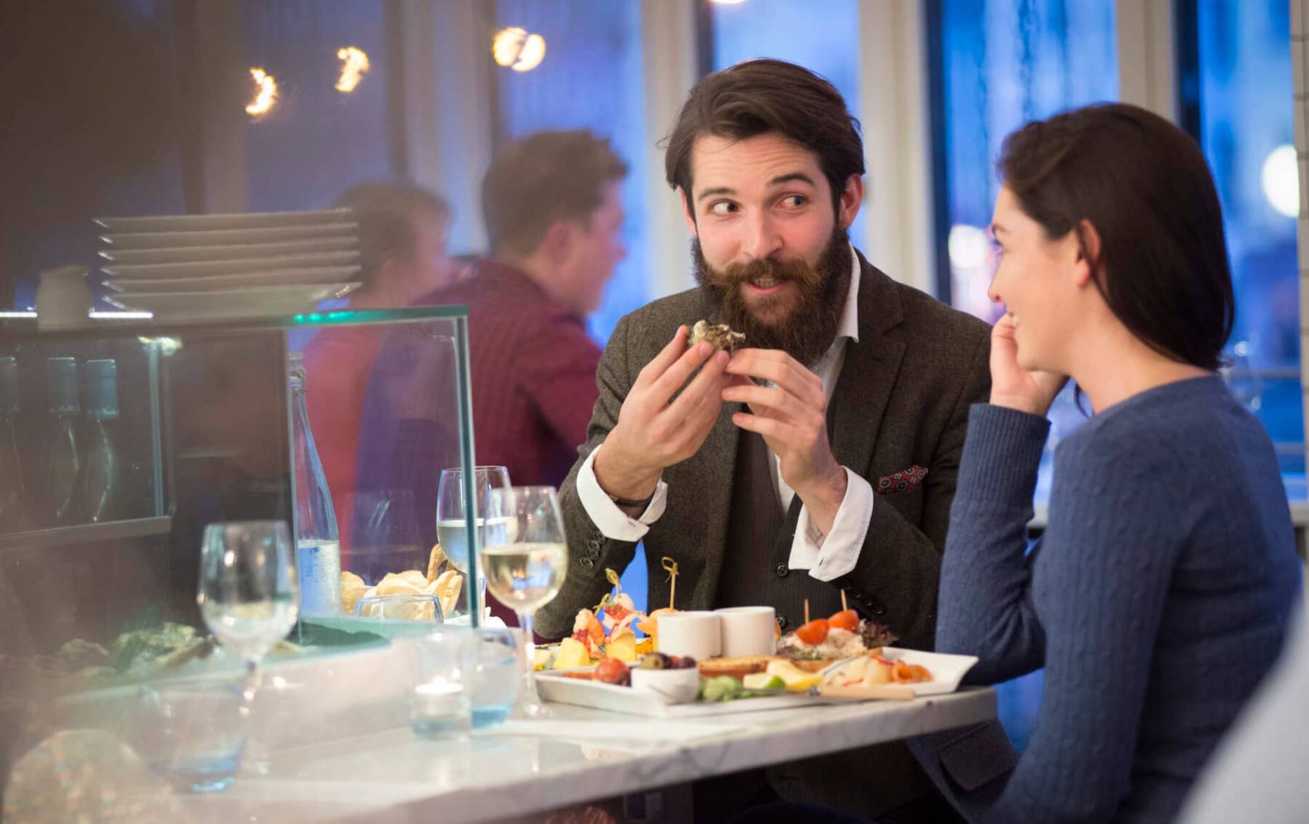 Un homme mangeant des huîtres et discutant avec une femme dans un restaurant de fruits de mer moderne à Cork, avec du vin sur la table.