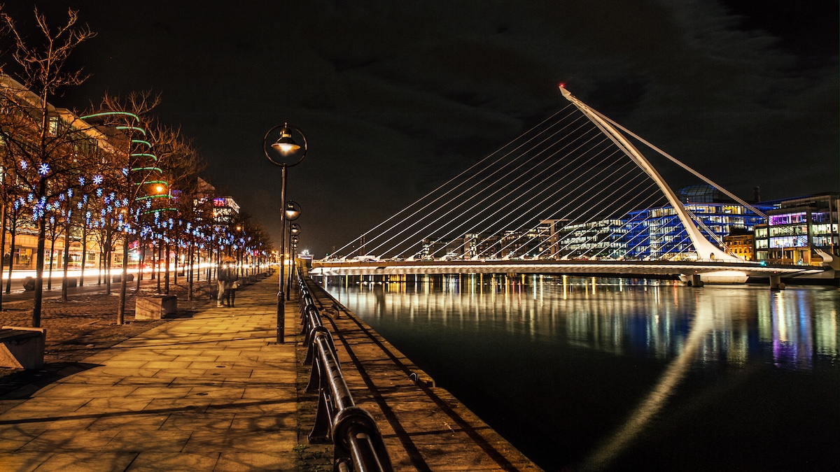 Samuel Beckett Bridge in Dublin erstrahlt nachts im Schein festlicher Weihnachtsbeleuchtung entlang des Flusses.