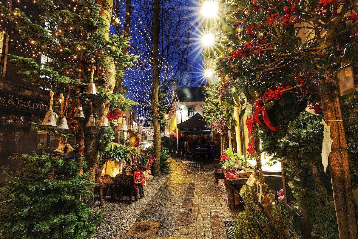 Festlich geschmückte Gasse in Galway mit Weihnachtskränzen, Lichtern und Marktständen.