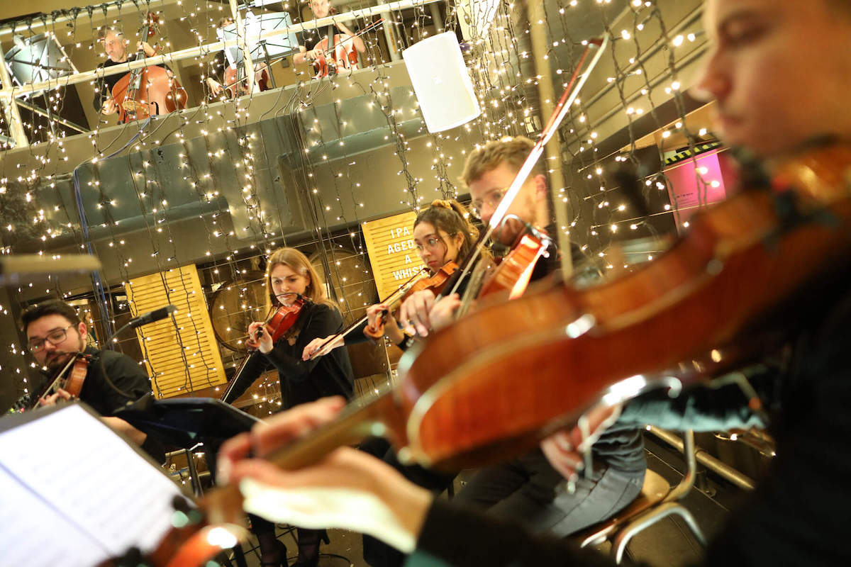 Musiker spielen Geigen und Celli unter festlichen Weihnachtslichtern im Guinness Storehouse, Dublin.