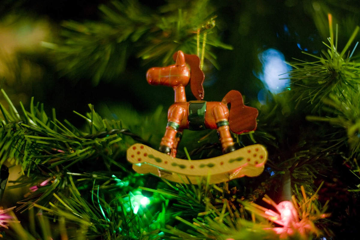 Nahaufnahme eines hölzernen Schaukelpferd-Weihnachtsbaumschmucks, der an einem geschmückten Baum hängt.