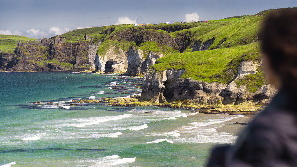 Blick über die Wellen auf die Burg Dunluce, die auf Klippen entlang der zerklüfteten Küste von Antrim in der Nähe von Portrush thront.