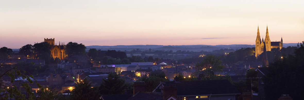 Veduta serale della città di Armagh, le sue due cattedrali illuminate si stagliano su un tramonto dai colori pastello.