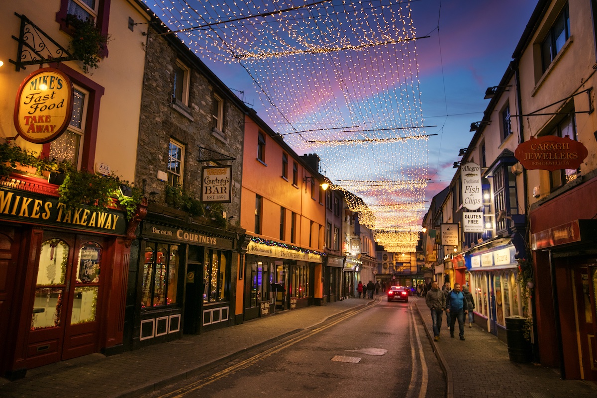 Straße in Killarney, geschmückt mit Weihnachtsbeleuchtung und gesäumt von Pubs und Geschäften.