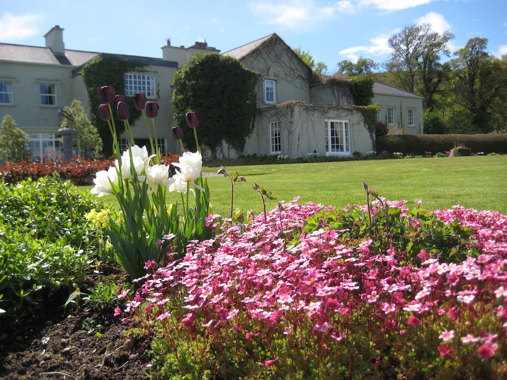Elegant Gregan's Castle in County Clare with manicured lawn and vibrant spring flowers in full bloom under blue skies.