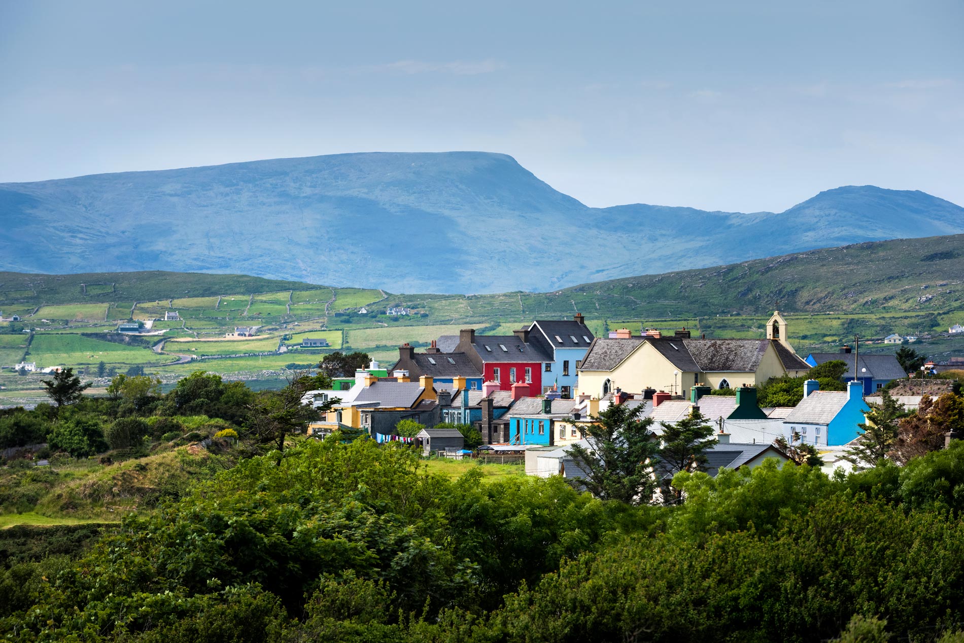 Kleurrijke huizen in het dorp Allihies liggen onder glooiende groene velden en ruige bergen op Ierlands Wild Atlantic Way.