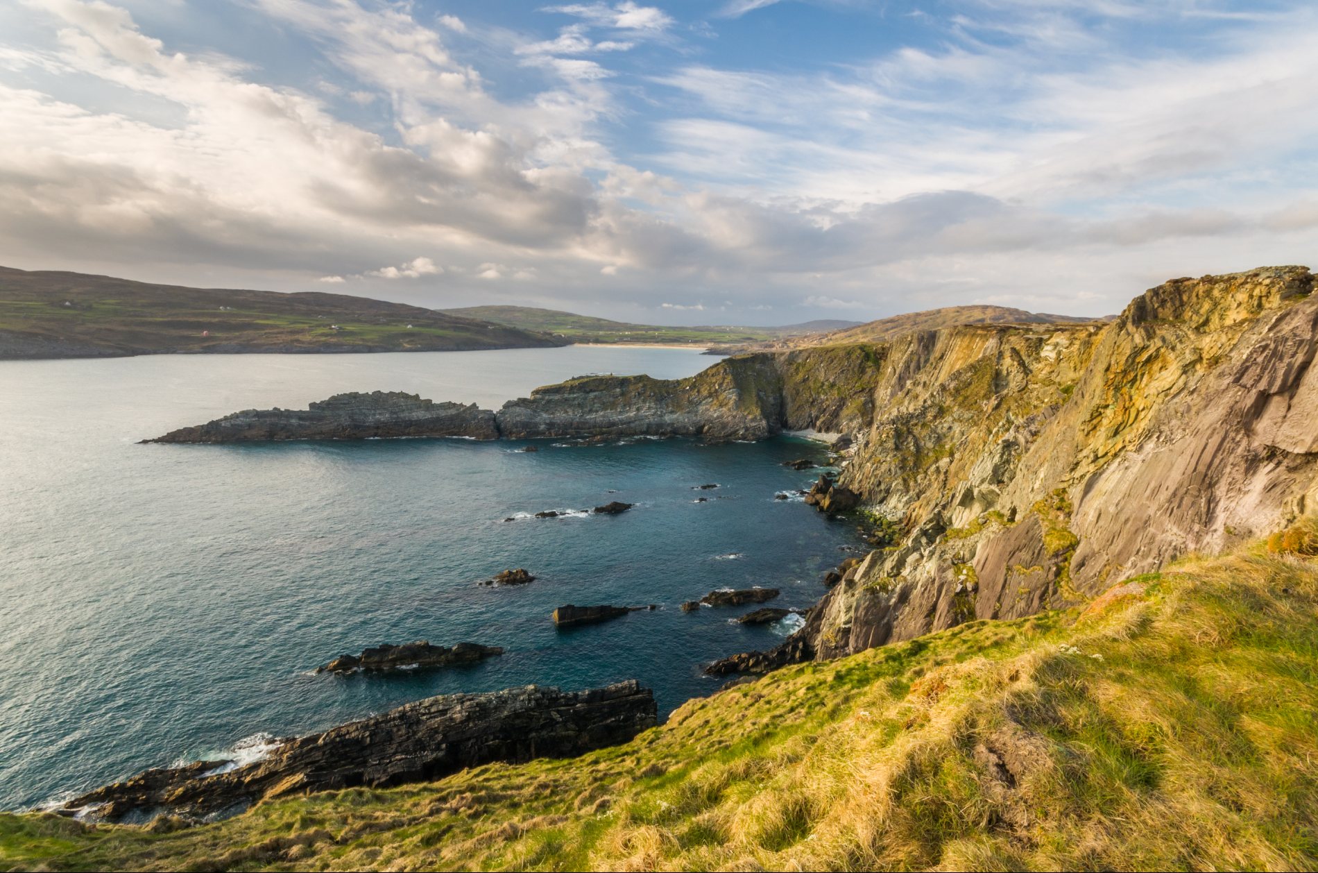Rotsachtige kustlijn bij Brow Head in West Cork, met grillige kliffen die de Atlantische golven onder een gedeeltelijk bewolkte lucht ontmoeten.