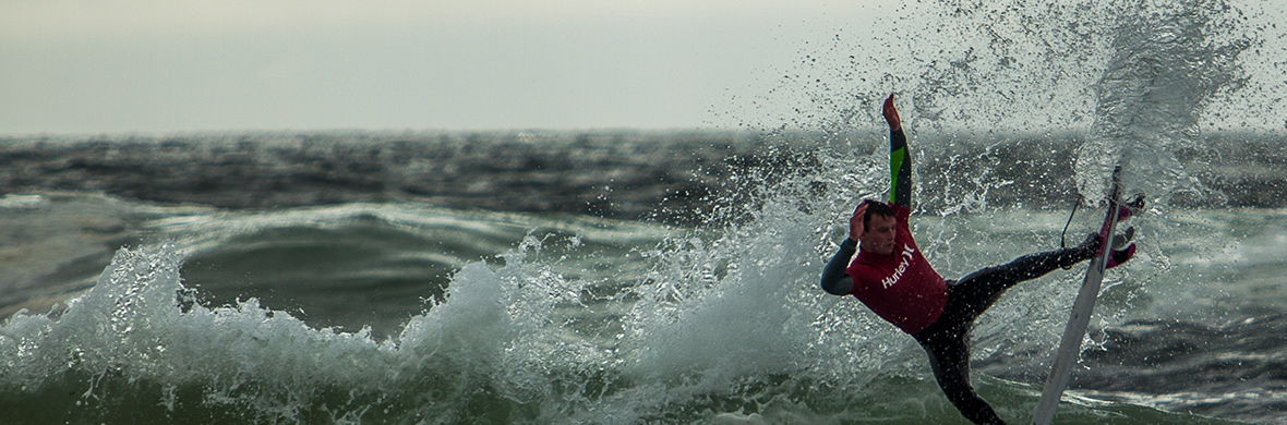 Surfeur en combinaison rouge tombant dans les airs depuis sa planche lors d'une chute sur les vagues agitées de l'Atlantique, dans le comté de Donegal.