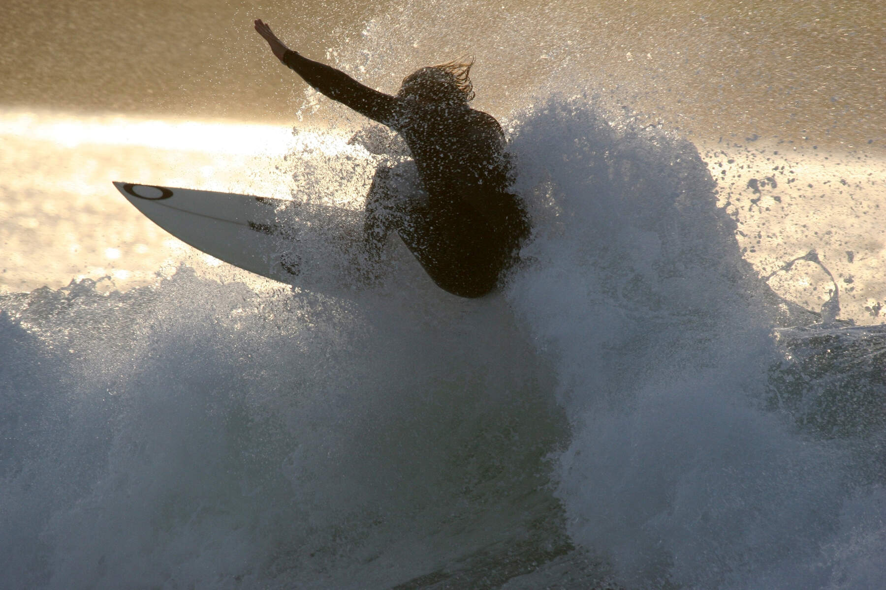 Silhouet van een surfer die midden in een draai op een krachtige golf bij Bundoran Beach in county Donegal staat, met zeewater dat rondom opspat.