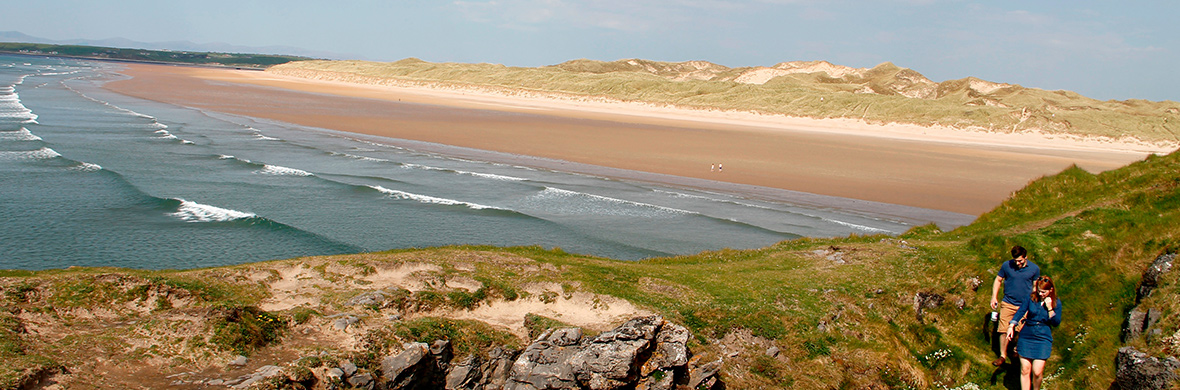 Des surfeurs marchent le long de la plage de Tullan près de Bundoran, dans le comté de Donegal, avec des vagues déferlant sur la plage de sable.