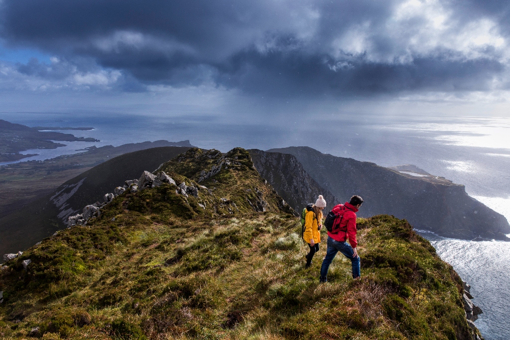 Twee wandelaars in heldere jassen op een pad langs de kliffen van Slieve League, met uitzicht op Donegal Bay.