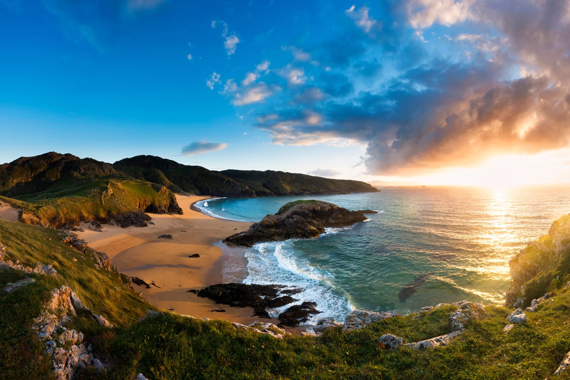 Blick auf den Murder Hole Beach im County Donegal zur goldenen Stunde, mit Klippen, türkisfarbenem Meer und sonnenbeschienenem Atlantikhorizont.