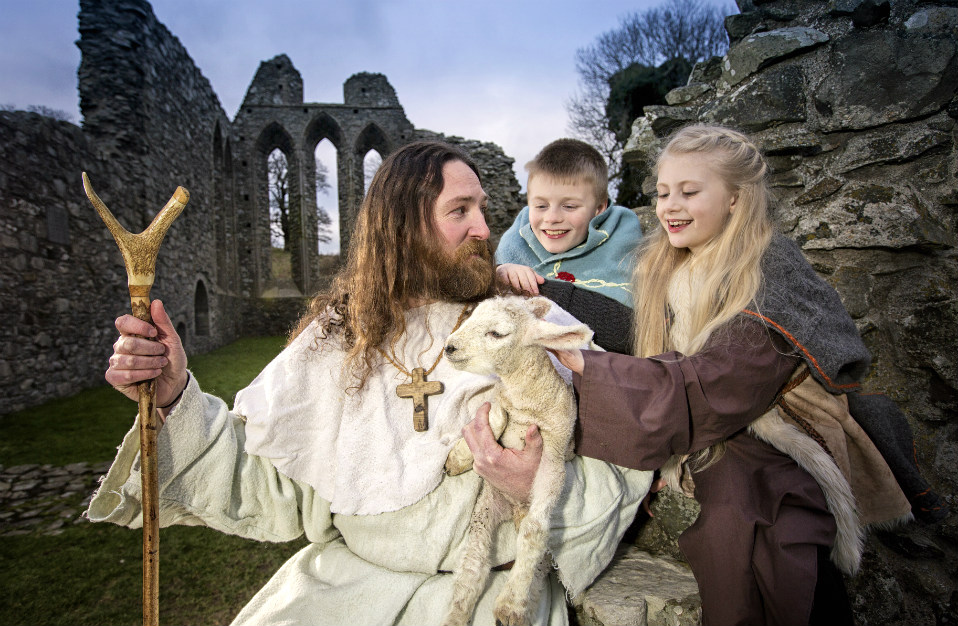 Een man verkleed als St. Patrick houdt een lam vast met kinderen bij de ruïne van Monasterboice in county Louth, Ierland.