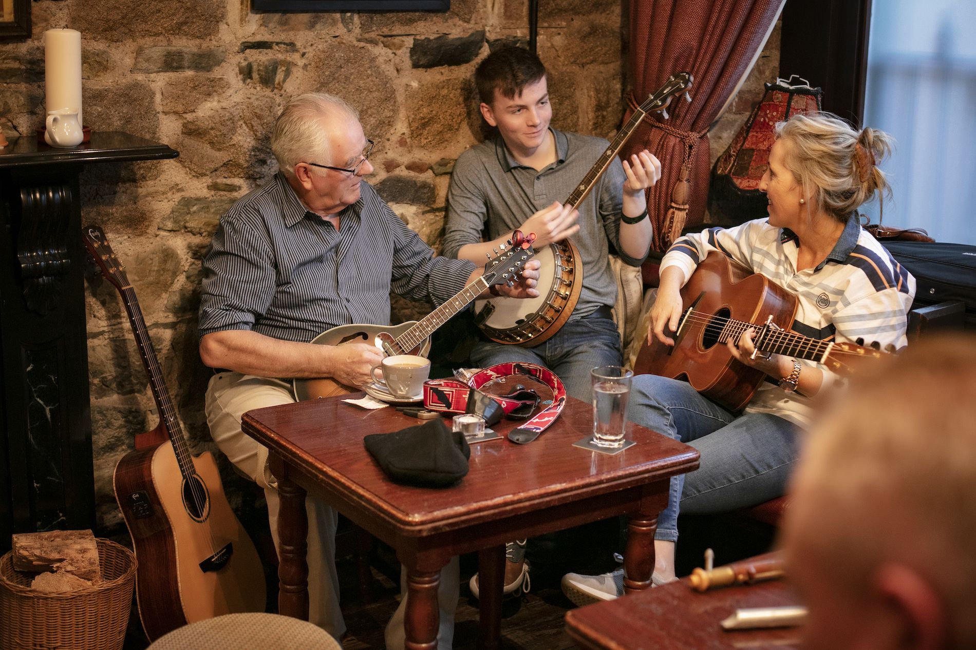 Drei Musiker sitzen in einem gemütlichen Pub und spielen während einer traditionellen irischen Musiksession Mandoline, Banjo und Gitarre.