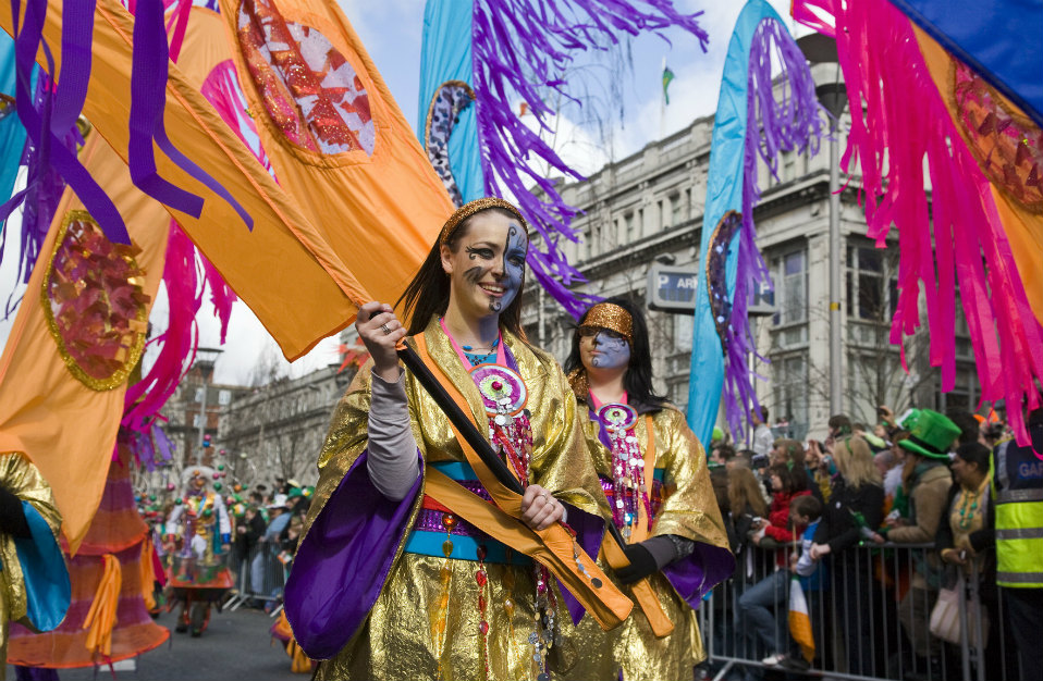 Deelnemers aan de parade in gouden kostuums dragen feloranje en paarse vlaggen tijdens de St. Patrick's Day in Dublin.