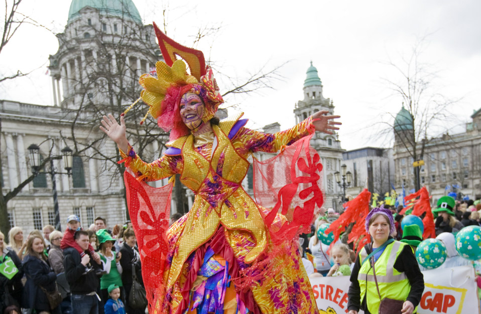 Een artiest in een kostuum met gouden en rode outfit vermaakt het publiek buiten het stadhuis van Belfast op St. Patrick's Day.