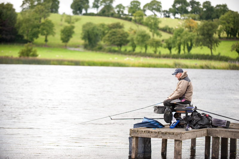 Angler at Lough Erne in Fermanagh, fishing peacefully from a wooden pier against calm waters and green hills.