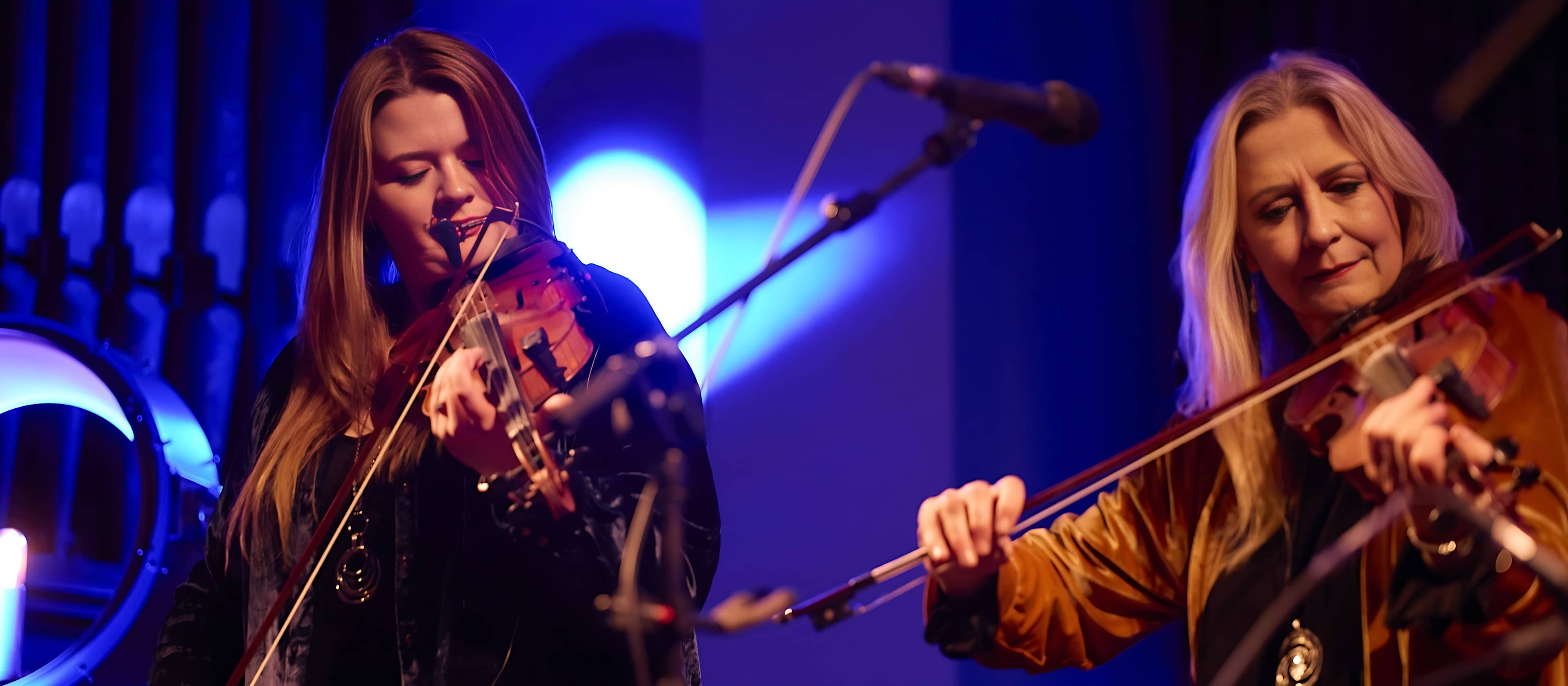 Two musicians from Altan play fiddles on stage under blue lighting during Tradfest, a live traditional Irish music festival in Dublin.