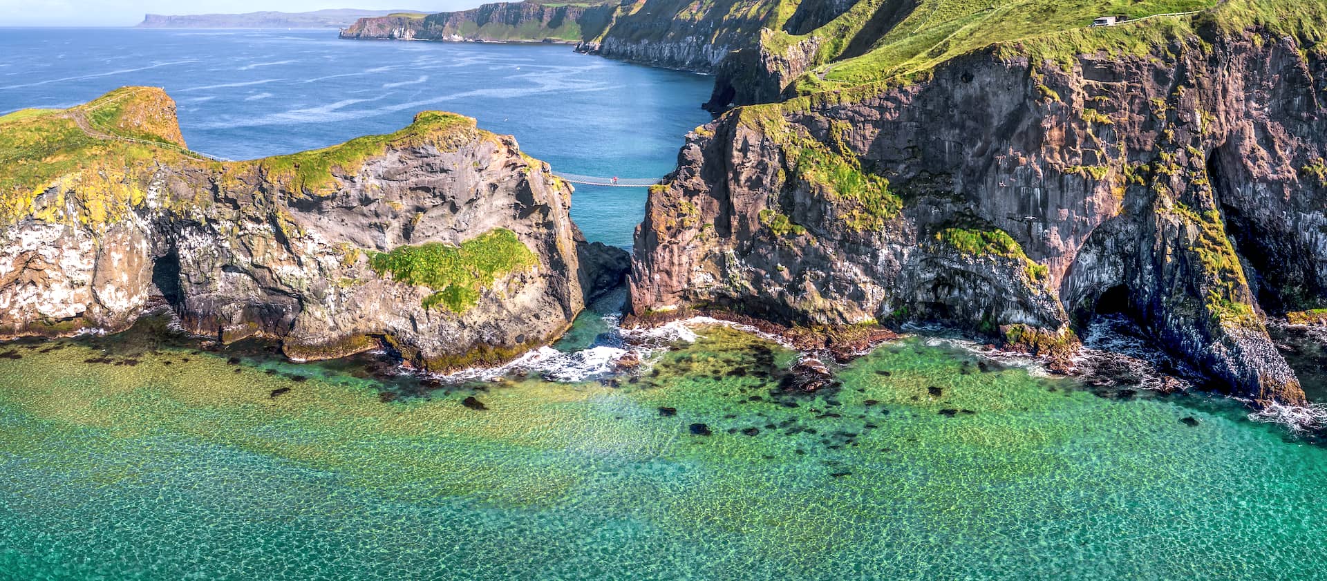 Carrick-a-Rede Rope Bridge spanning sea cliffs above clear turquoise water on the Antrim Coast, Northern Ireland.