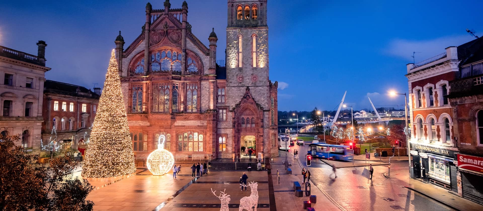 The Guildhall lit at Christmas with a tall glowing tree, festive lights and people walking through the square at dusk.