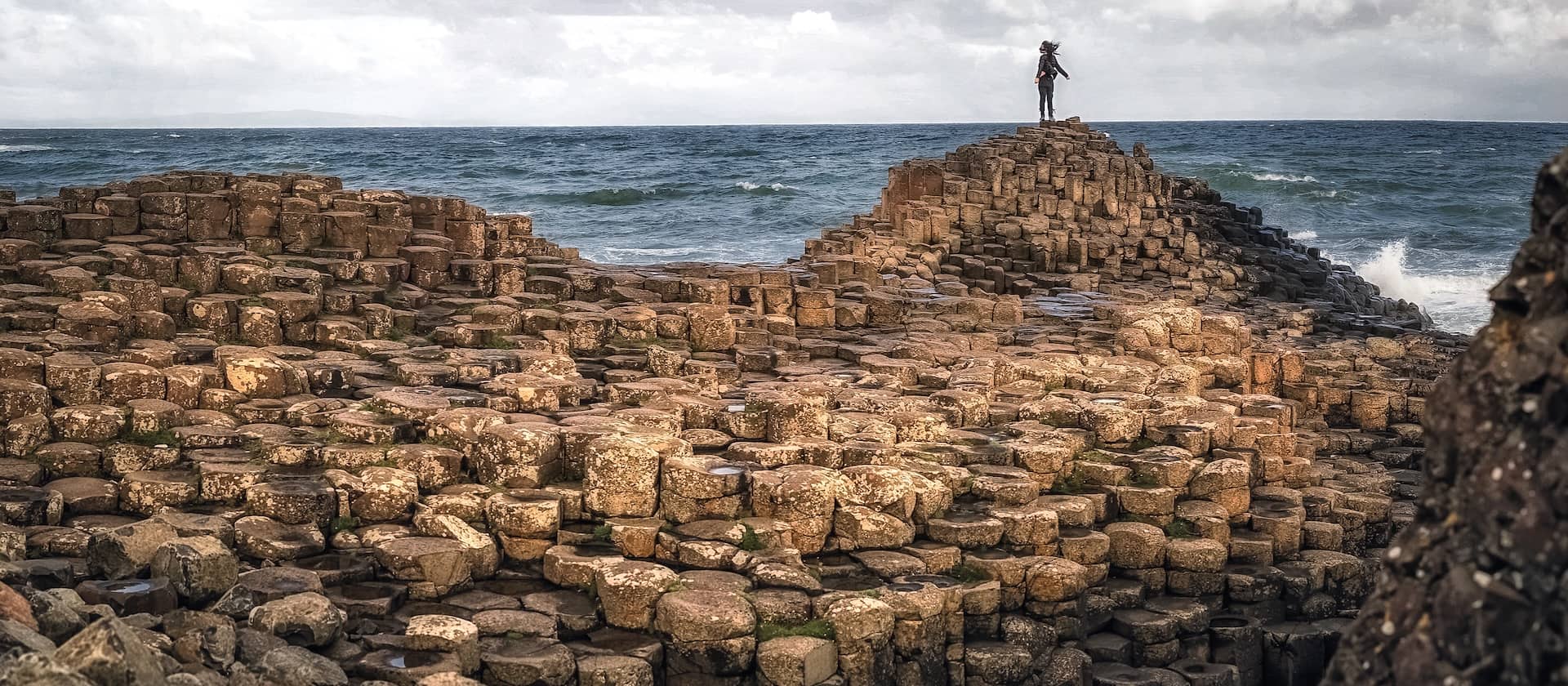 Visitor standing on the Giant’s Causeway basalt columns, County Antrim coastal landmark.