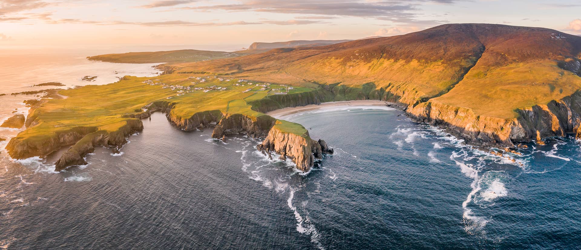 Aerial view of Silver Strand beach in County Donegal with rugged cliffs, rolling hills and Atlantic coastline at sunset.