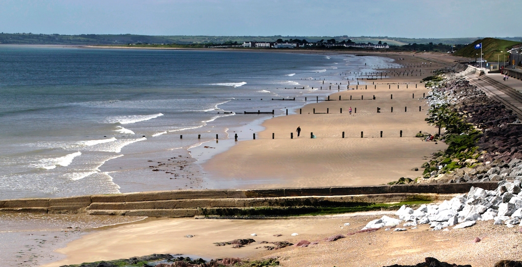 Sandy beach in County Cork with wooden groynes stretching into the sea and people walking along the shoreline.
