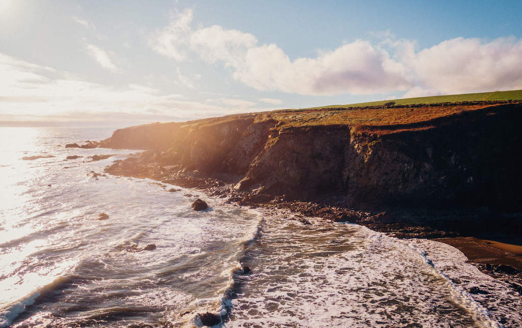 Rugged coastal cliffs with waves crashing below at sunset along the Copper Coast in County Waterford.