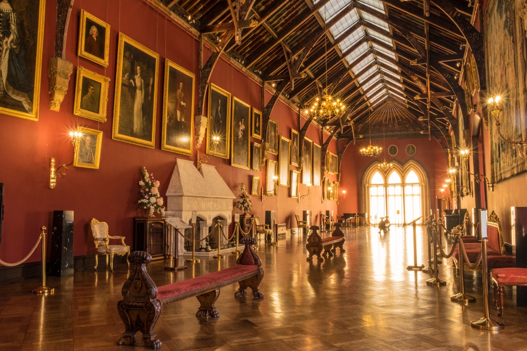 Galerij met rode muren in het kasteel van Kilkenny, met portretten in gouden lijsten, kroonluchters en gepolijste parketvloeren.