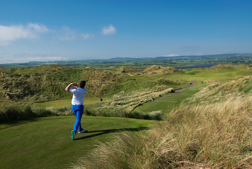 A golfer tees off at Portstewart Golf Club, framed by sweeping dunes and panoramic countryside views.