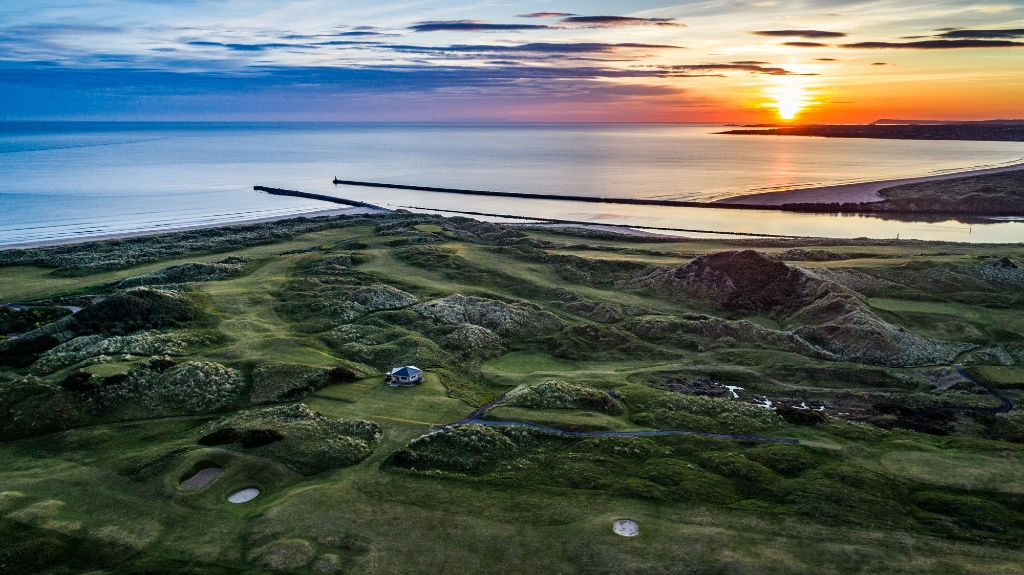 Sunset over Portstewart Strand, golden light illuminates rolling dunes and the vast links course by the shore.