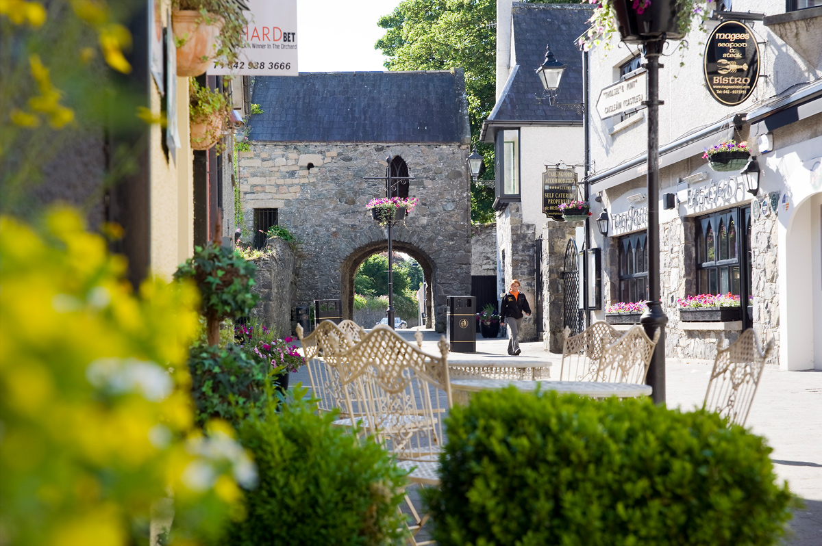 Café tables line a quaint flower-filled laneway leading to a medieval gatehouse in the coastal town of Carlingford.