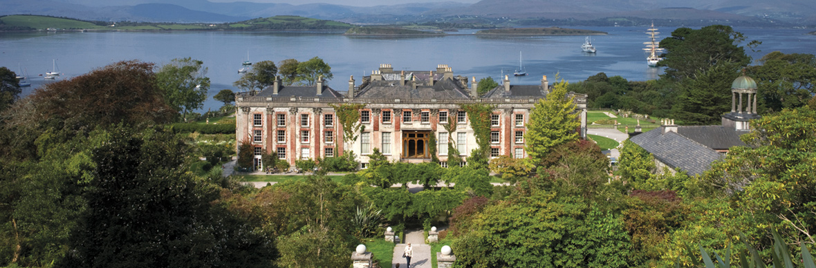 Das historische Bantry House, umgeben von Gärten und Bäumen, mit der Bantry Bay und Segelbooten im Hintergrund, Grafschaft Cork.