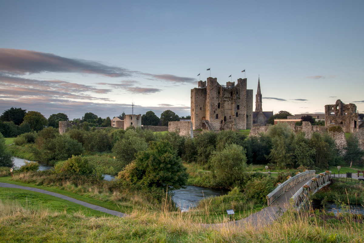 View of Trim Castle with flags flying above its keep, surrounded by greenery and the River Boyne.