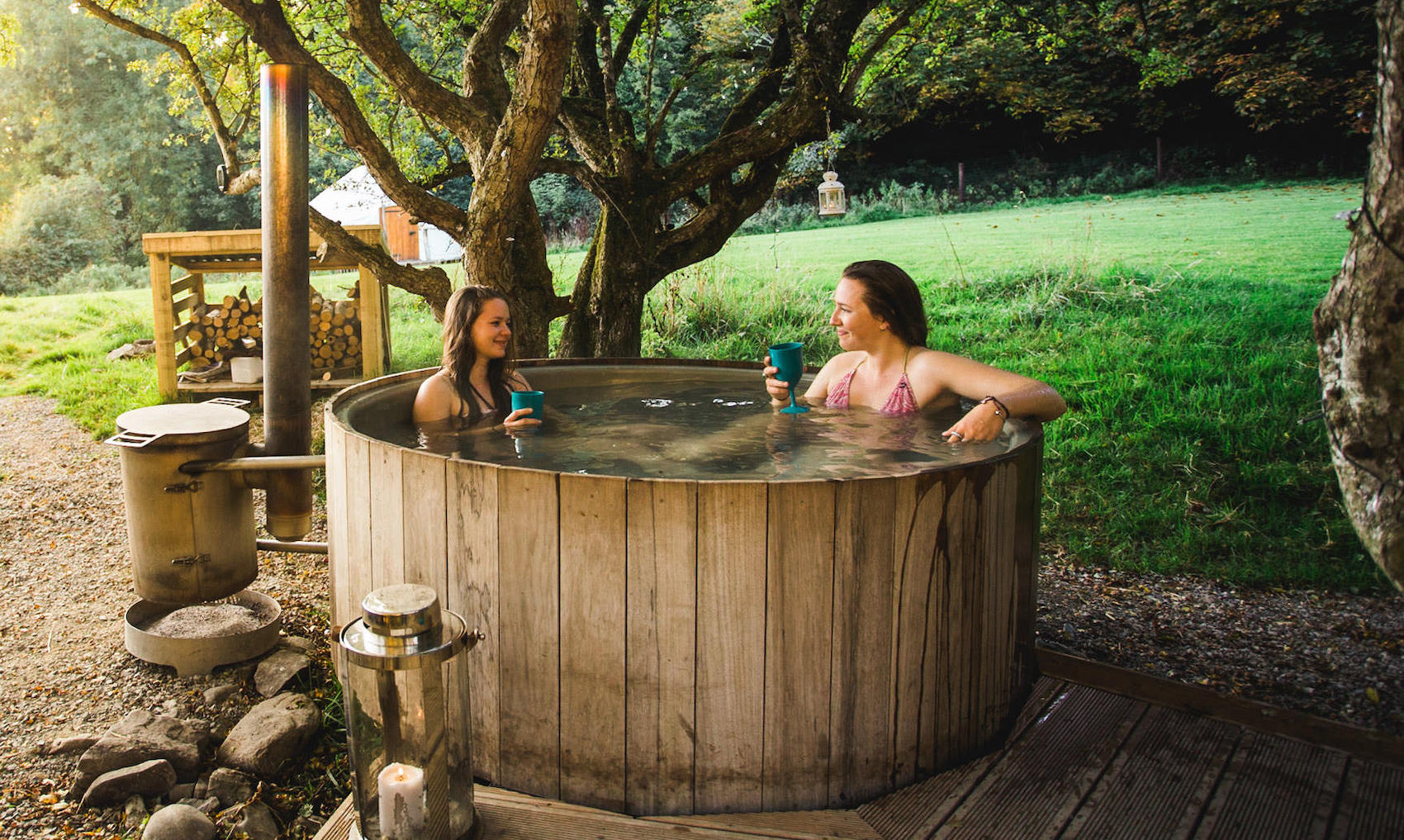 Two women relaxing in an outdoor wooden hot tub at Rock Farm Slane, County Meath, surrounded by nature and trees.