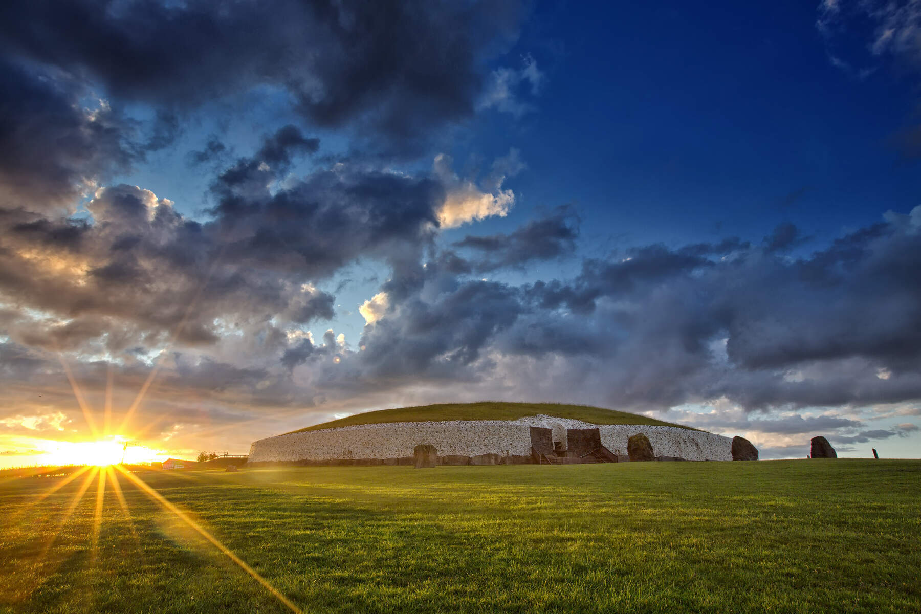 Amanecer invernal que proyecta una luz dorada sobre el túmulo cubierto de hierba y la entrada de piedra de Newgrange.