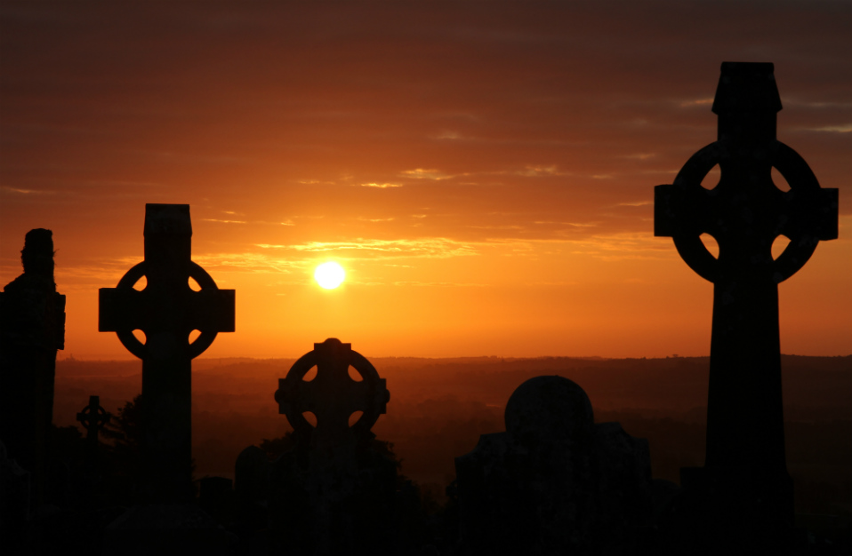 Keltische kruisen als silhouetten tegen een gloeiende oranje zonsondergang in Ierland.