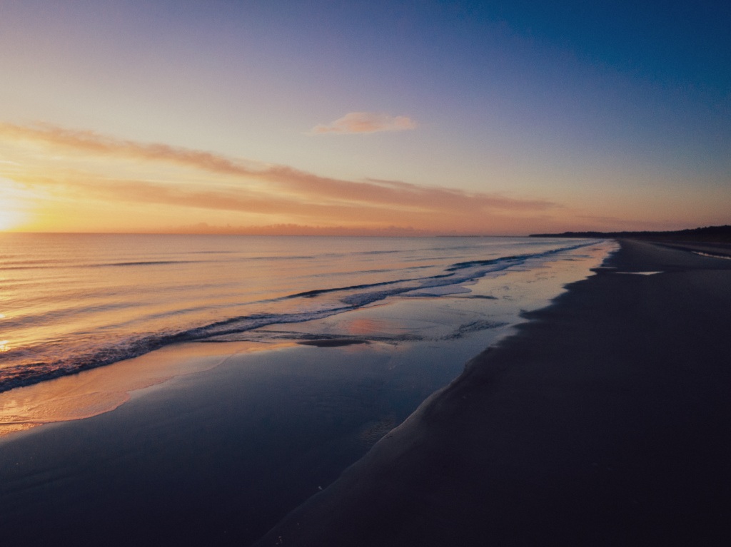 Goldener Sonnenuntergang über dem Curracloe Beach in der Grafschaft Wexford, Irland, mit ruhigen Wellen, die den Strand berühren.