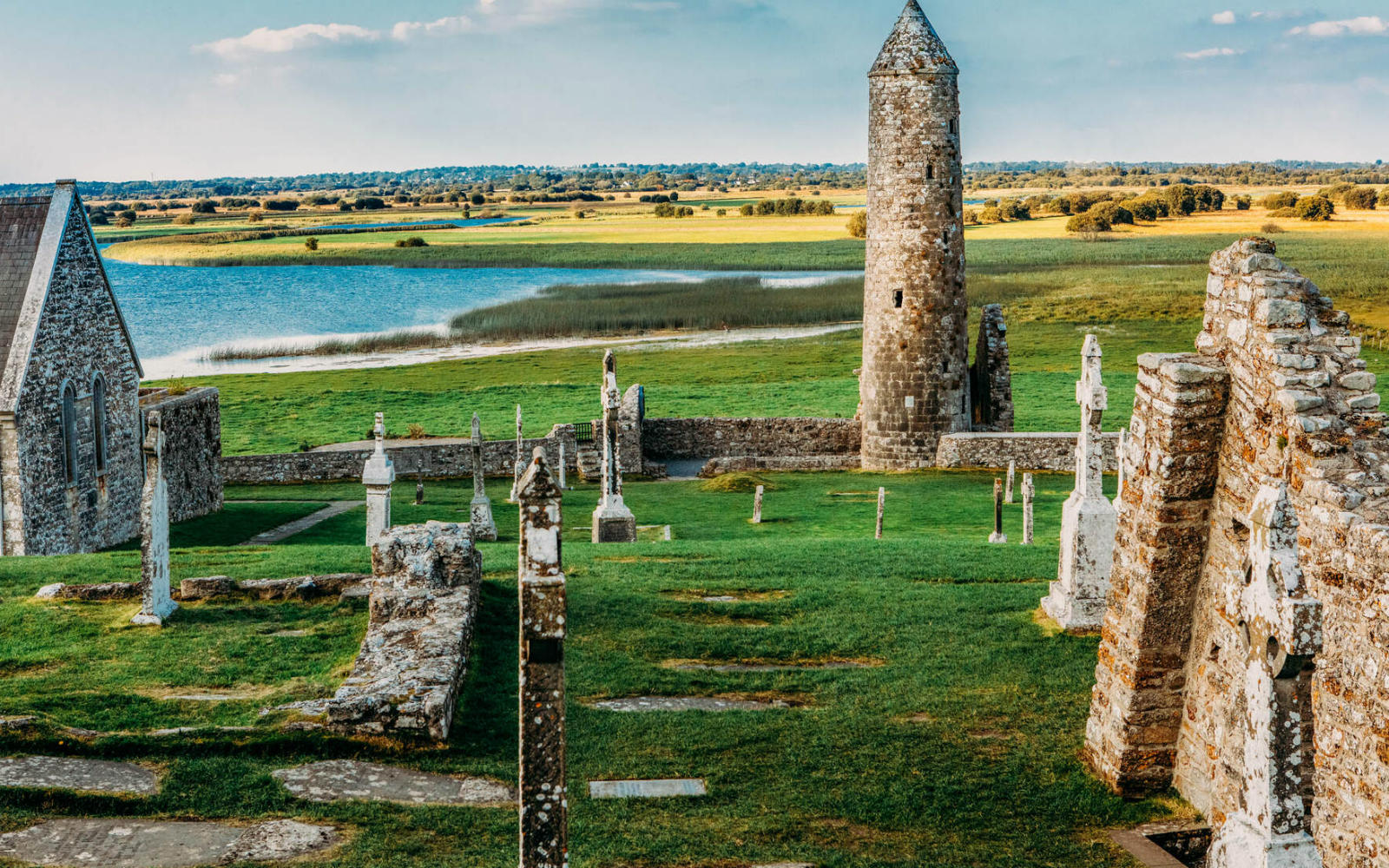 Ruins of Clonmacnoise Monastery with stone crosses and a round tower overlooking the River Shannon, County Offaly.