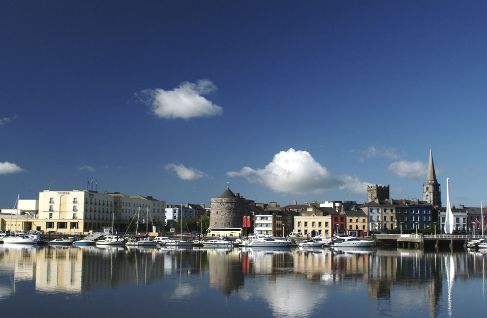 Boats moored along Waterford’s historic quay with Reginald’s Tower and church spires visible.