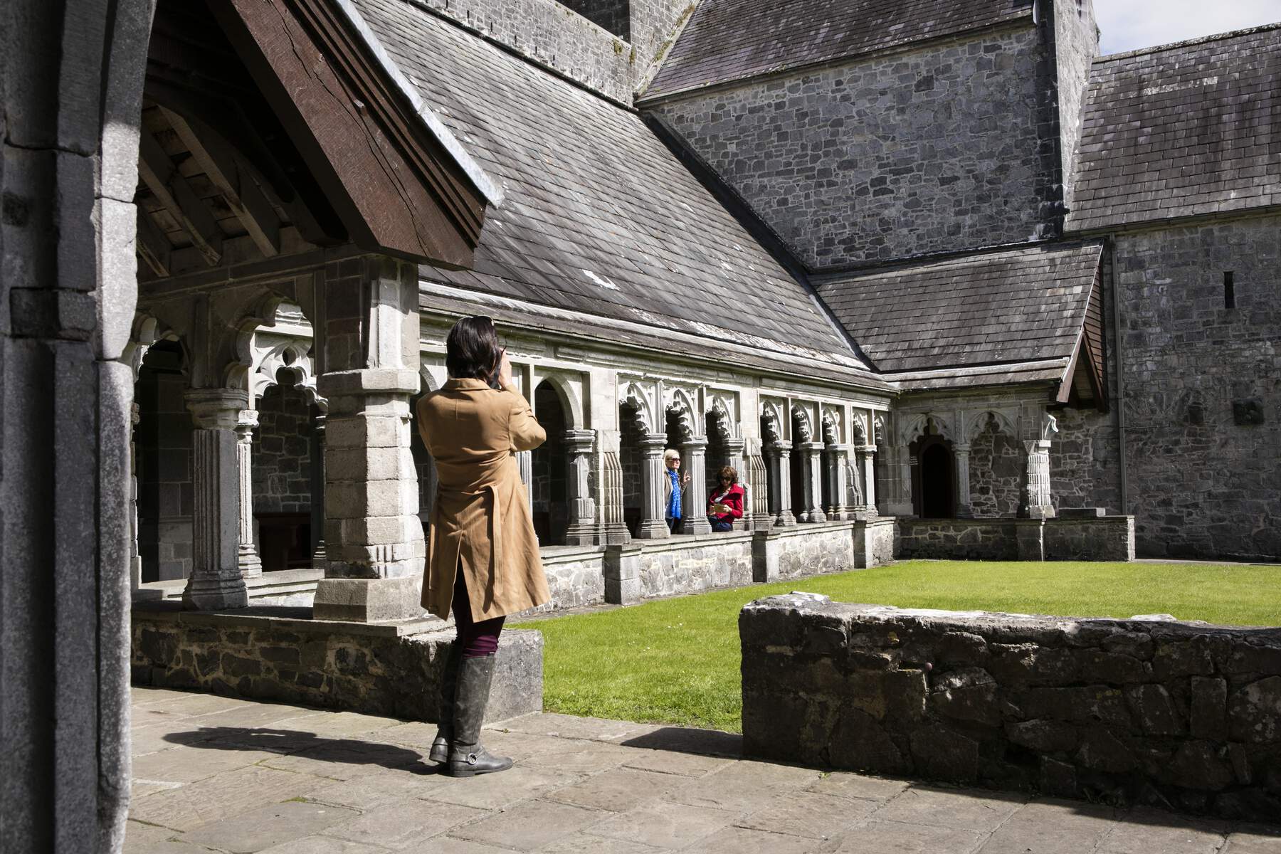 Visiteur prenant des photos à l'intérieur de l'abbaye de Sainte-Croix avec des cloîtres en pierre et une architecture médiévale, comté de Tipperary.
