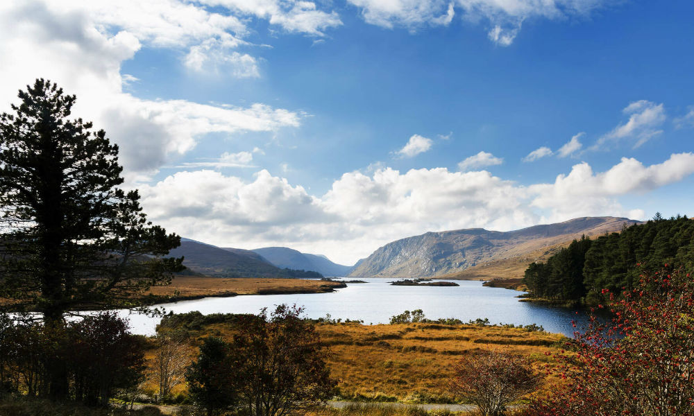 Weite Aussicht auf den See von Glenveagh, das Tal und die umliegenden Hügel unter einem mit flauschigen weißen Wolken gespickten Himmel.