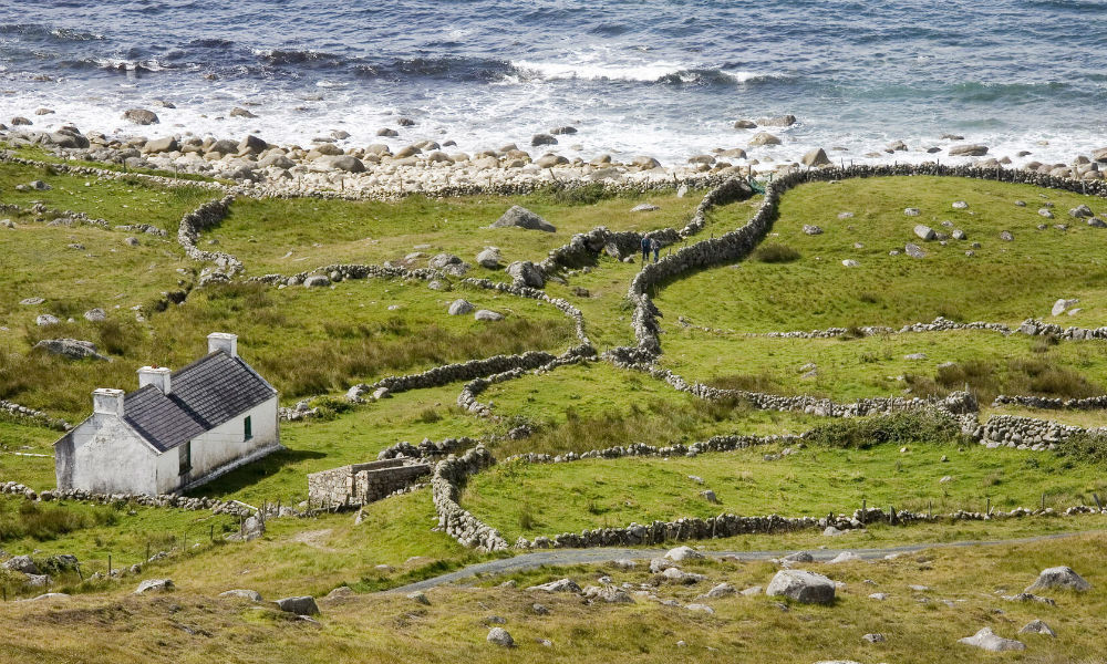 Weiß getünchtes Cottage, umgeben von gewundenen Stein-Mauern und felsigen grünen Feldern in Bloody Foreland.