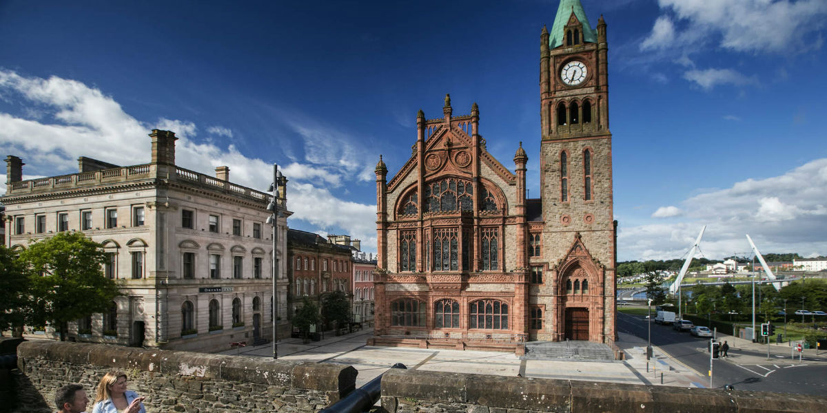 Die rote Backsteinfassade und der Uhrenturm des Guildhall ragen unter dem blauen Himmel in der Stadt Derry~Londonderry empor.