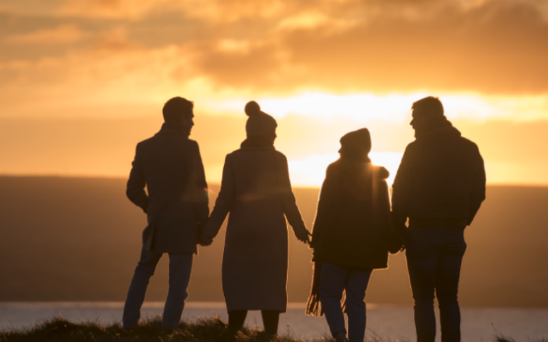 Silhouetted friends walk hand-in-hand along Portstewart Strand at sunset, framed by golden light.