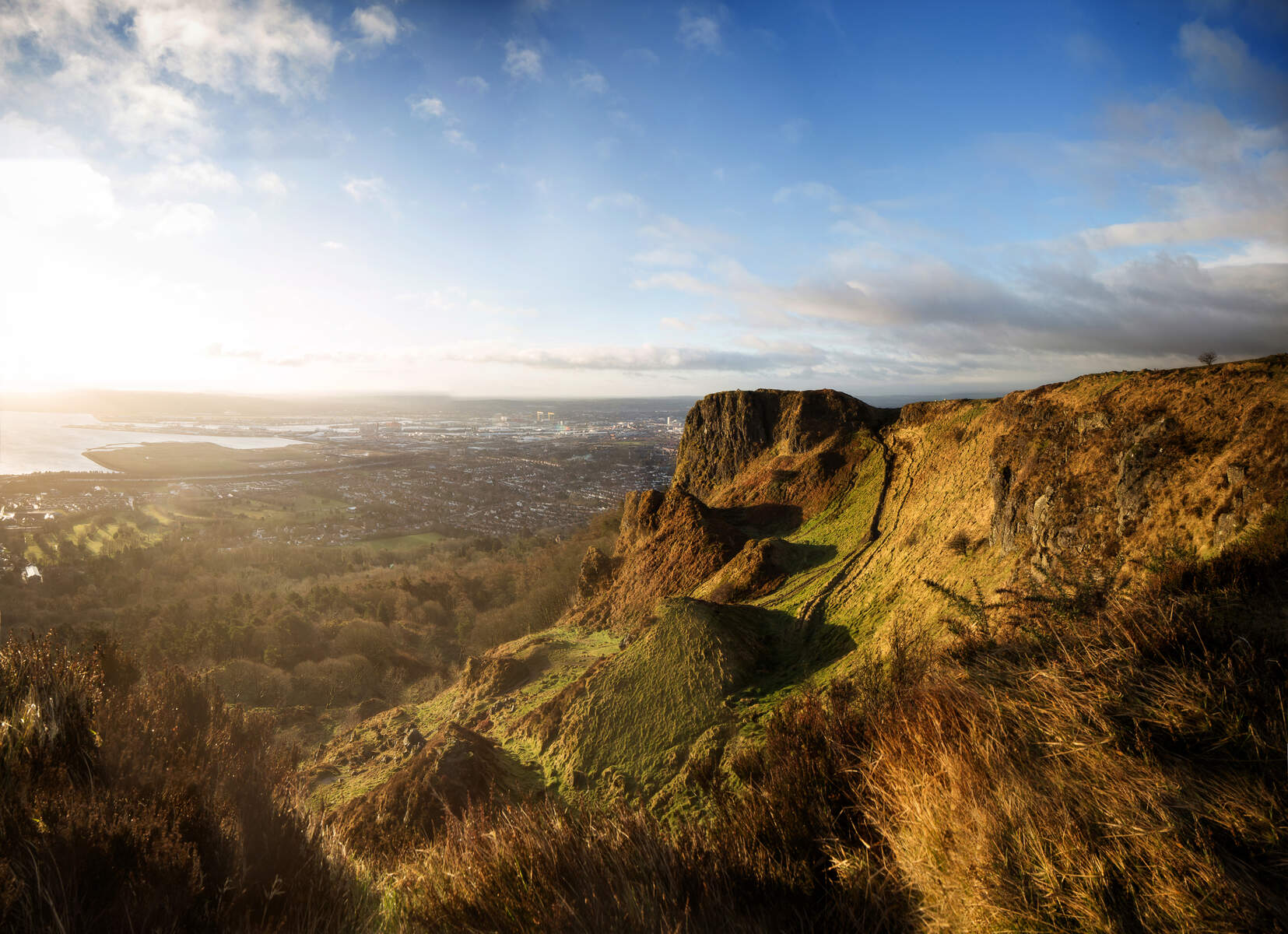 Il sole della sera illumina la Cave Hill di Belfast mentre si affaccia sulla città e sul Lough con le sue spettacolari scogliere dorate e le verdi pendici.