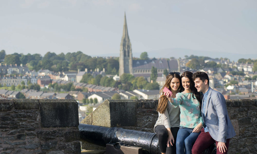 Drei Freunde posieren für ein Selfie neben einer Kanone auf den historischen 17th-century Stadtmauern von Derry~Londonderry.