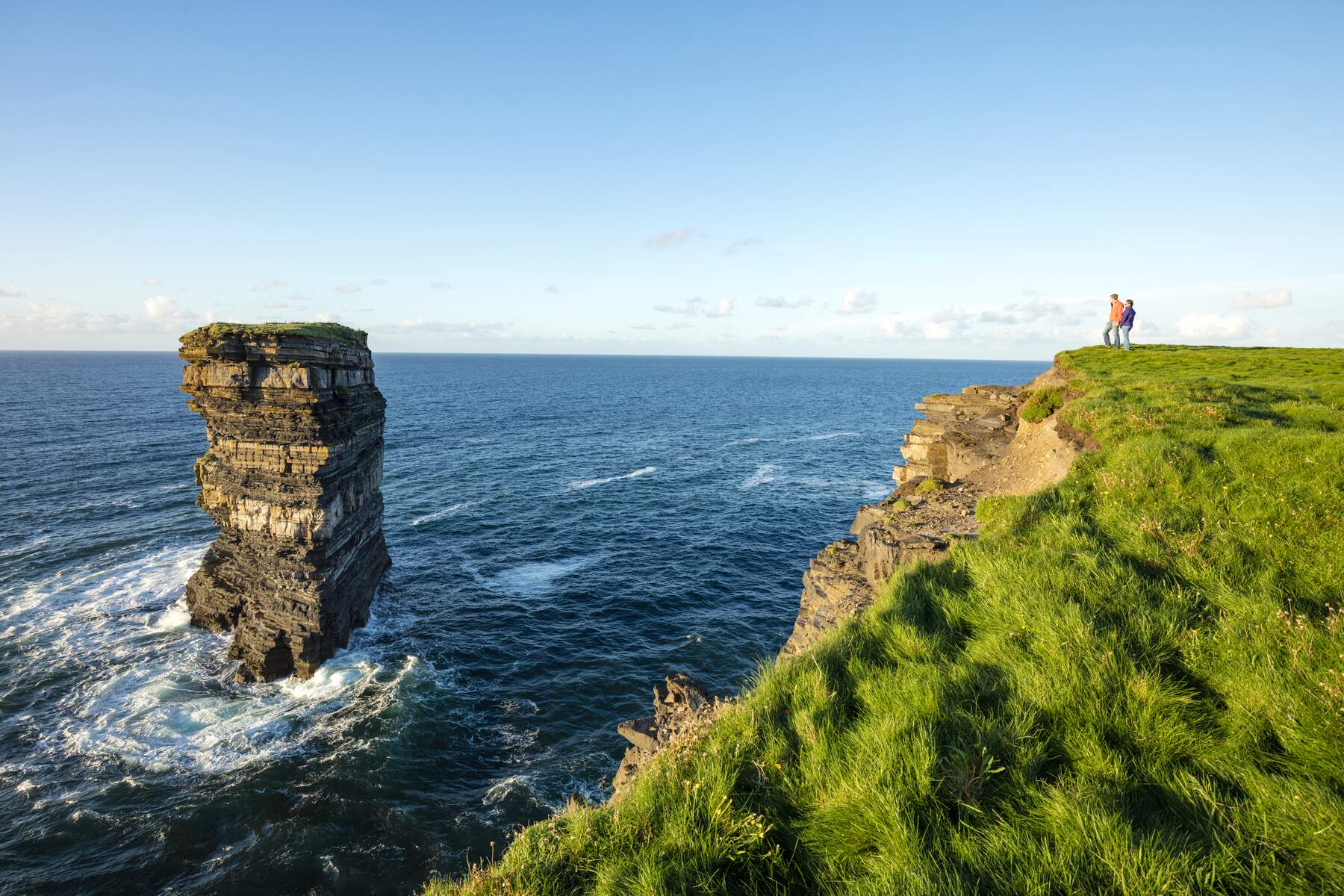 Un couple se tient près de la falaise herbeuse Berge surplombant l'impressionnante pile marine de Dún Briste à Downpatrick Head.