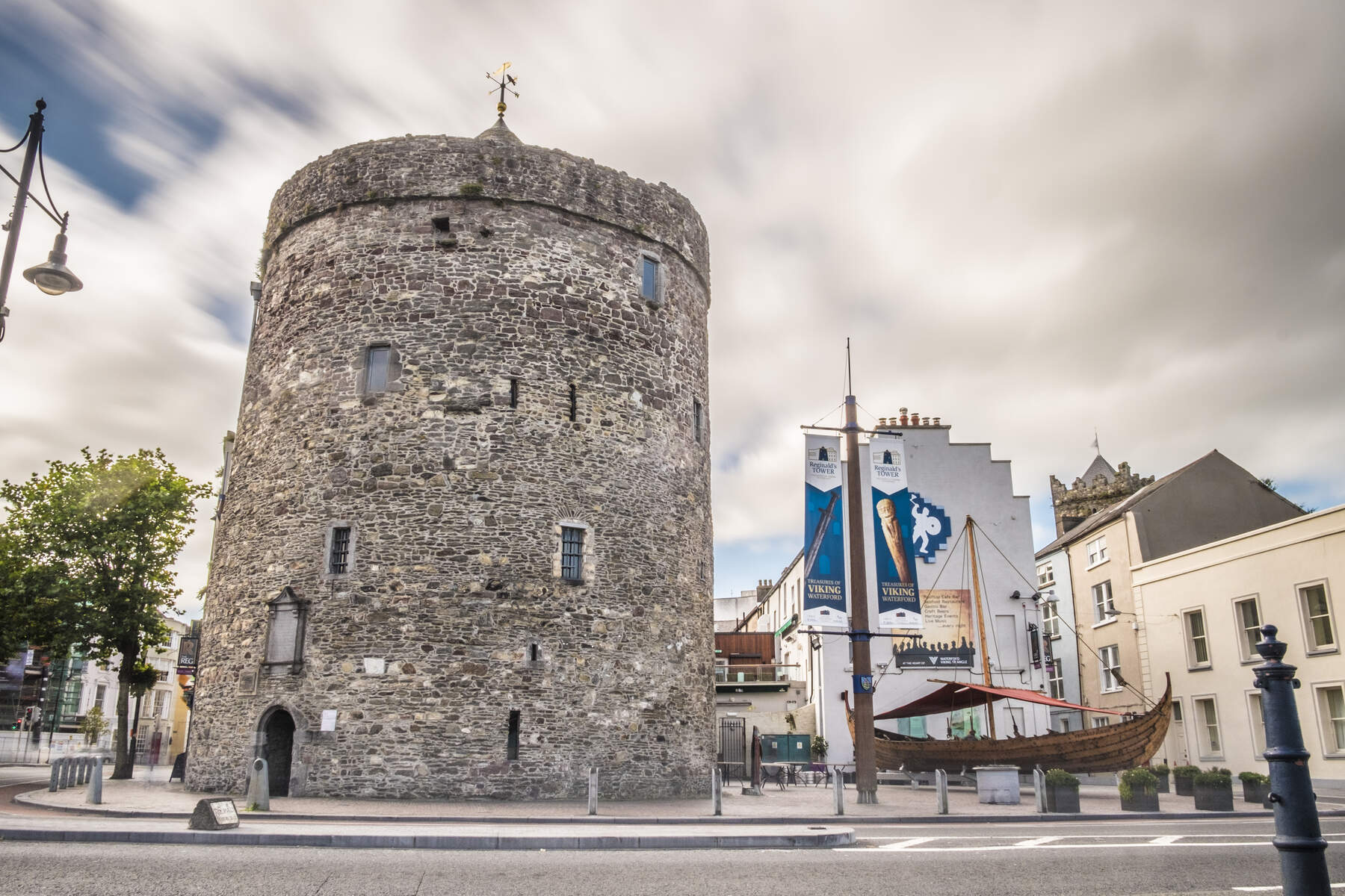 Cirkelvormige stenen toren bekend als Reginald's Tower in Waterford, naast een tentoonstelling van Vikingschepen en erfgoedvlaggen.